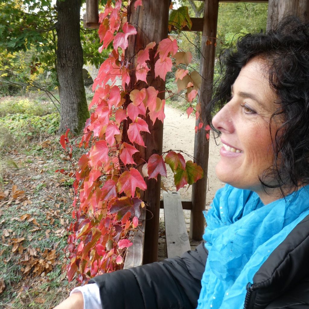 Silvia Grum in der Natur neben einer Holzpergola mit rot gefärbtem Herbstlaub